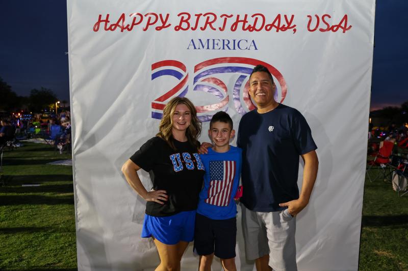 photo of family in front of Happy Birthday USA America 250 sign at a park 